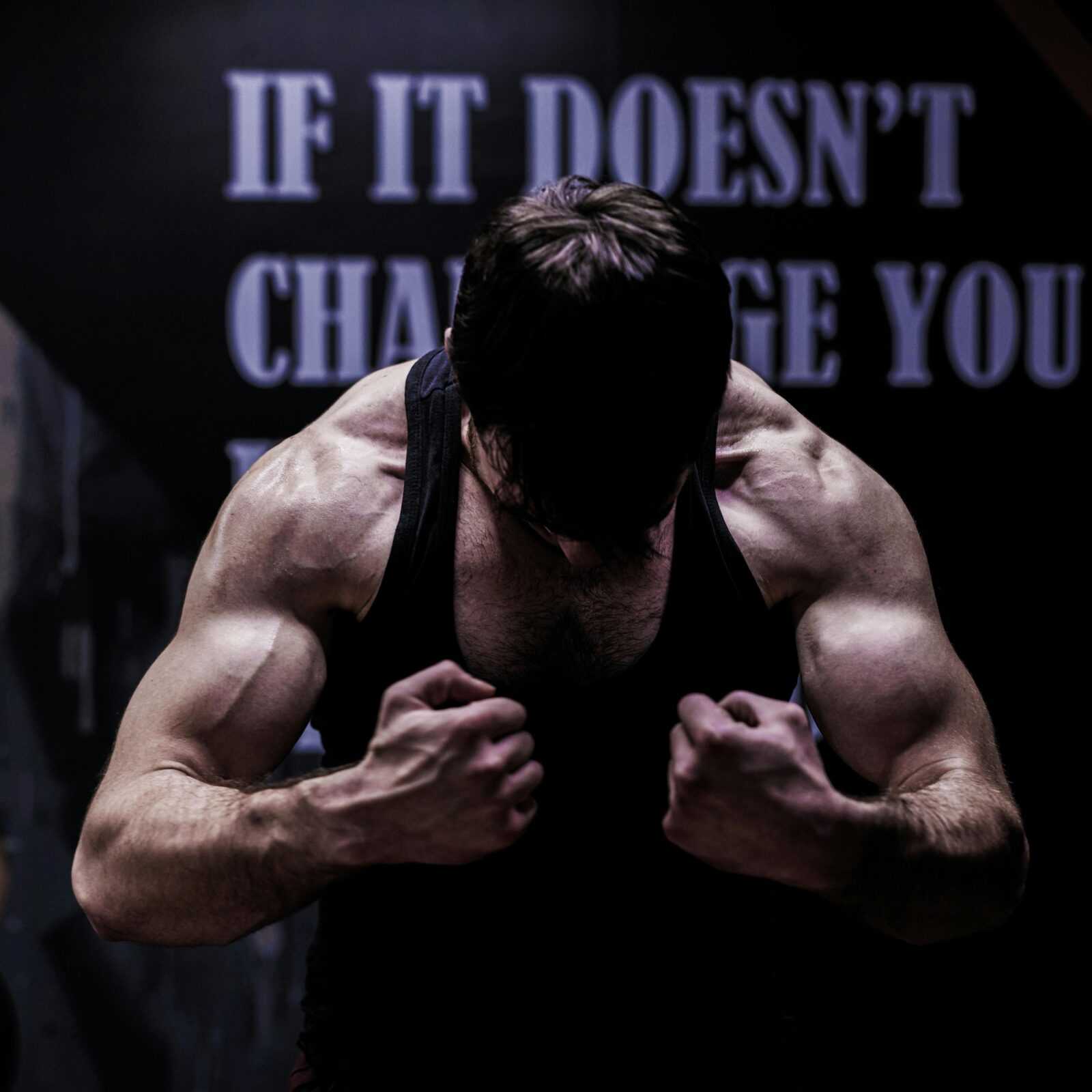 Muscular male bodybuilder posing in a dimly lit gym, showcasing strength and dedication.