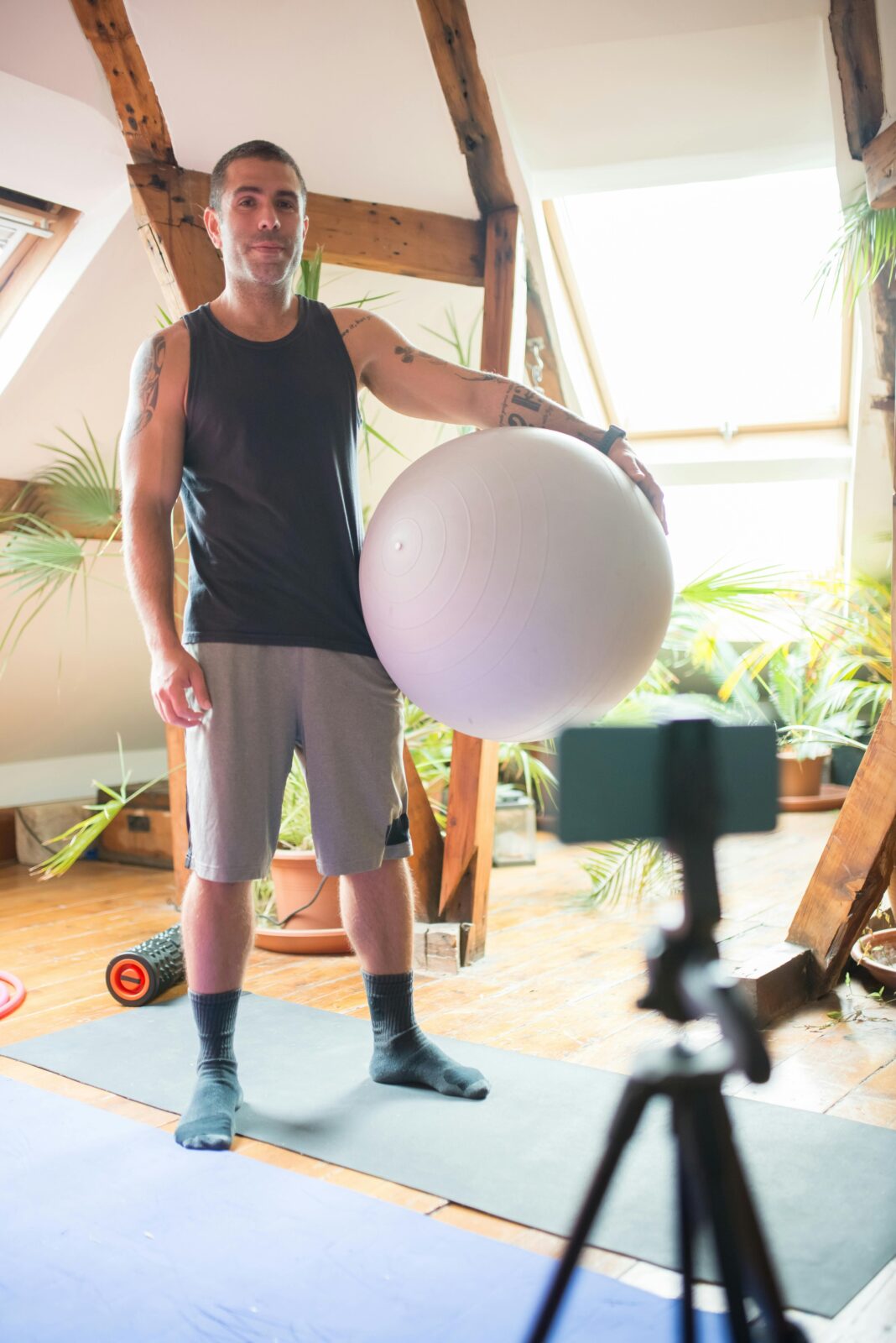 Man in sportswear filming a home workout with a yoga ball, perfect for fitness blogs.
